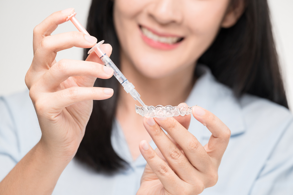 A woman applying gel in her teeth whitening trays