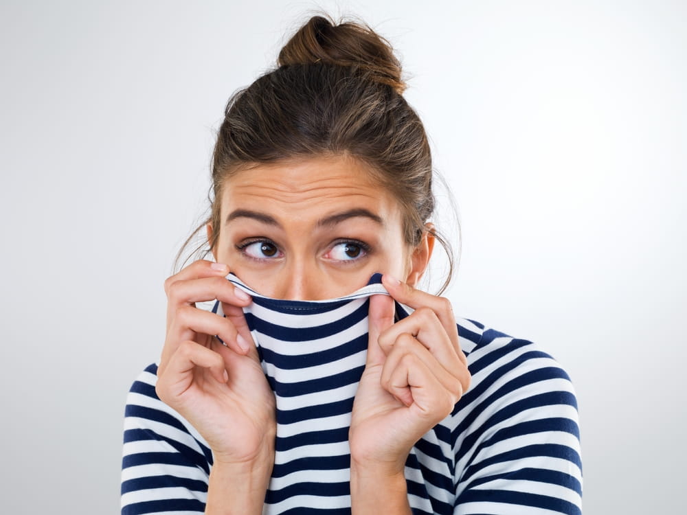Une femme cache son sourire avec son chandail car elle a honte ne pas avoir consulté le dentiste pendant longtemps